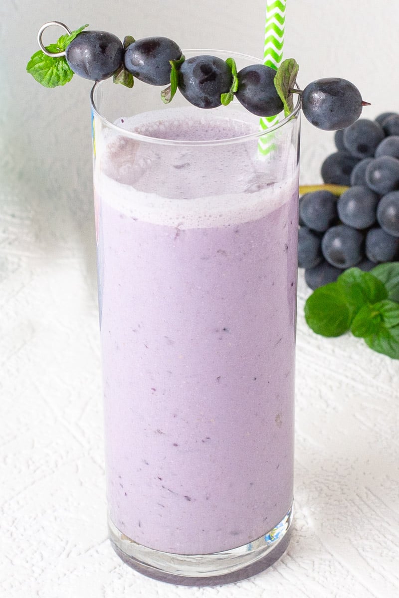 Tall glass of grape smoothie with steel cut oats. Garnished with concord grapes.