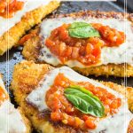 Cast iron skillet with chicken cutlets topped with marinara sauce melted cheese and fresh basil leaf.