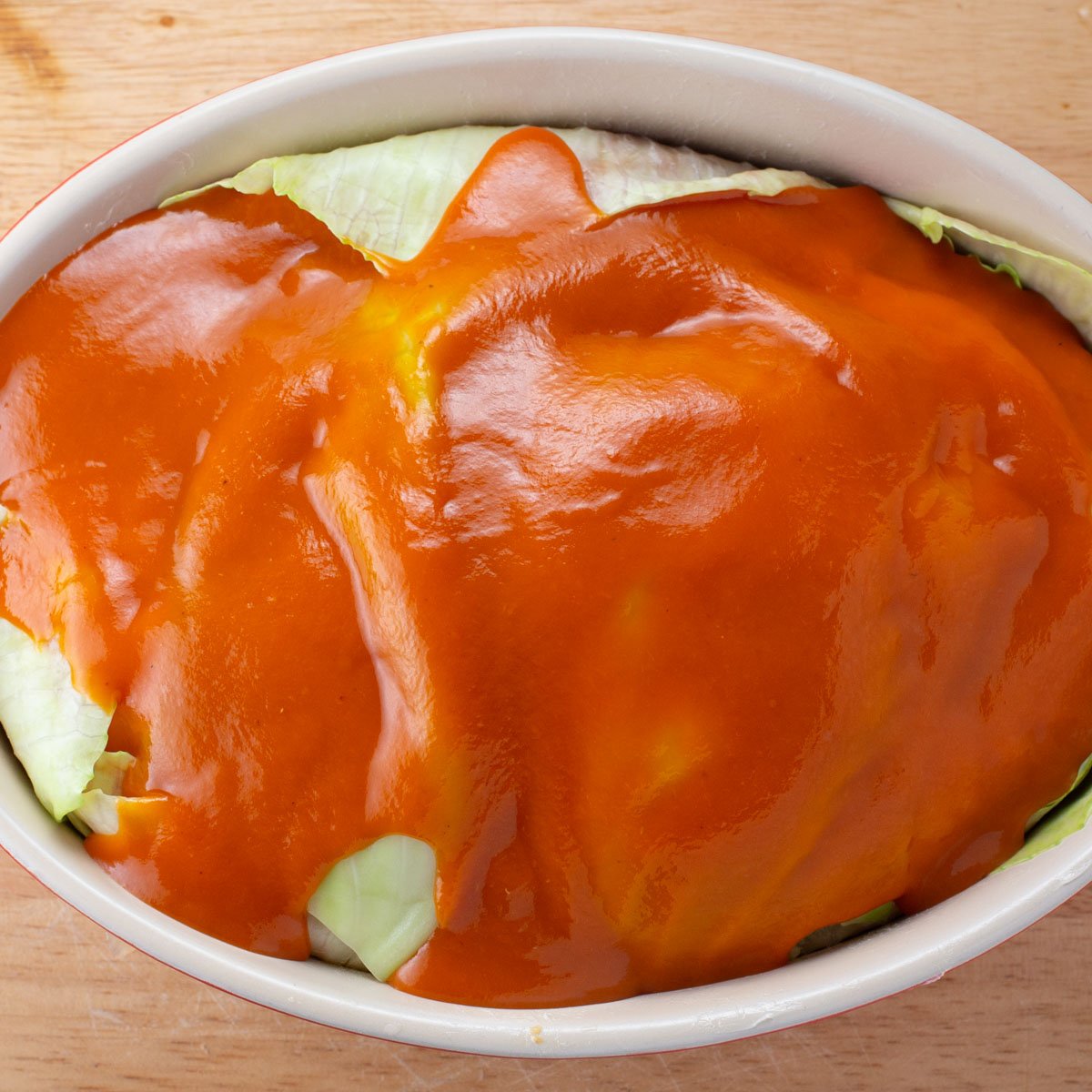 Uncooked casserole of cabbage and ground turkey covered in tomato sauce.