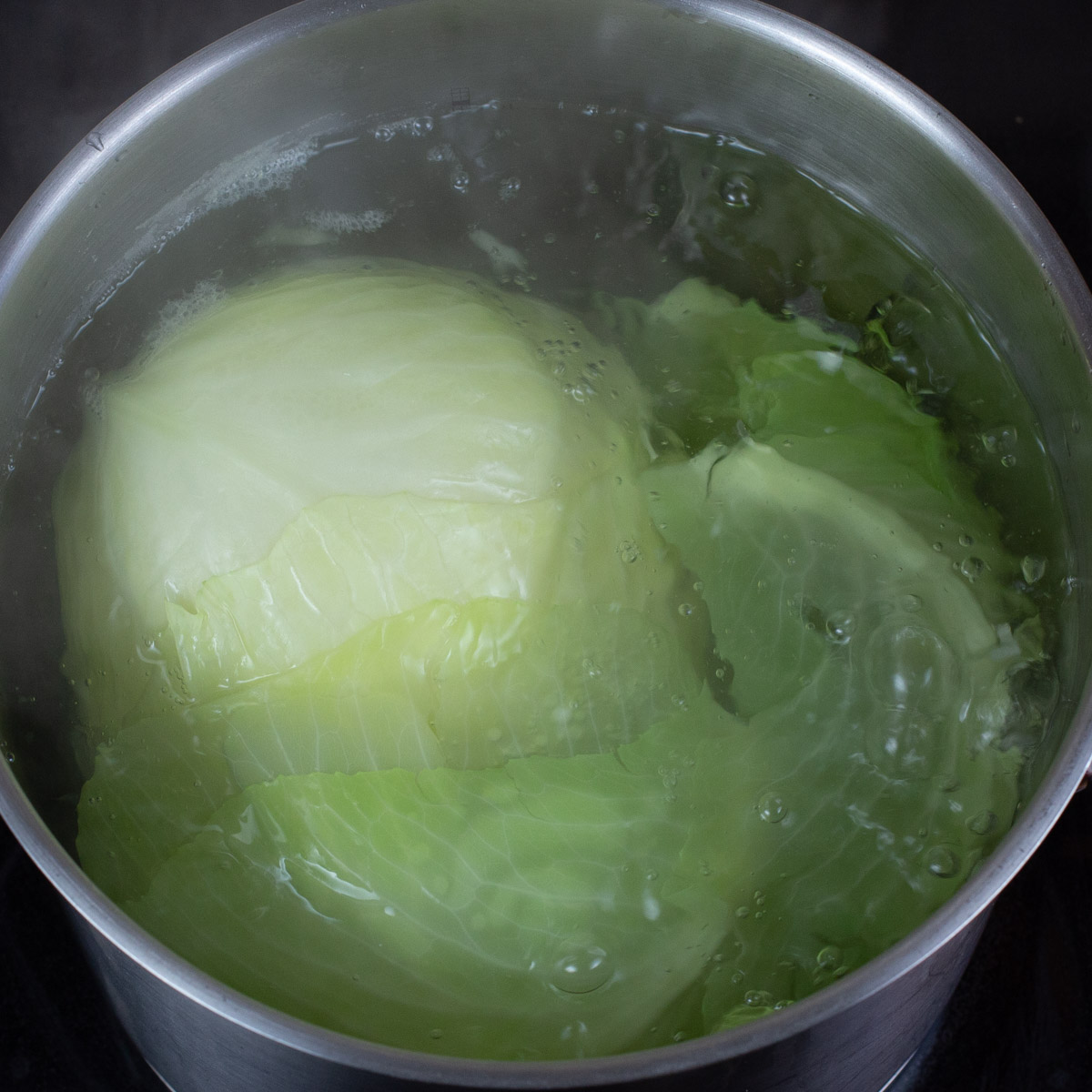 Whole cabbage boiling in stainless steel pot.