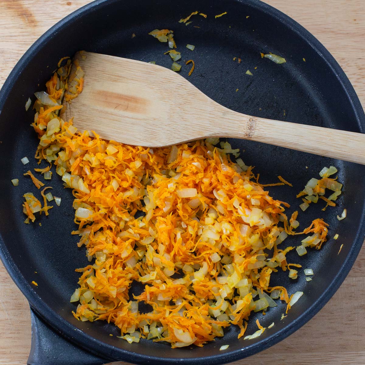 Black skillet with sautéed carrots and onions.