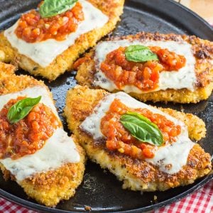 Cast iron skillet with chicken cutlets topped with marinara sauce melted cheese and fresh basil leaf.