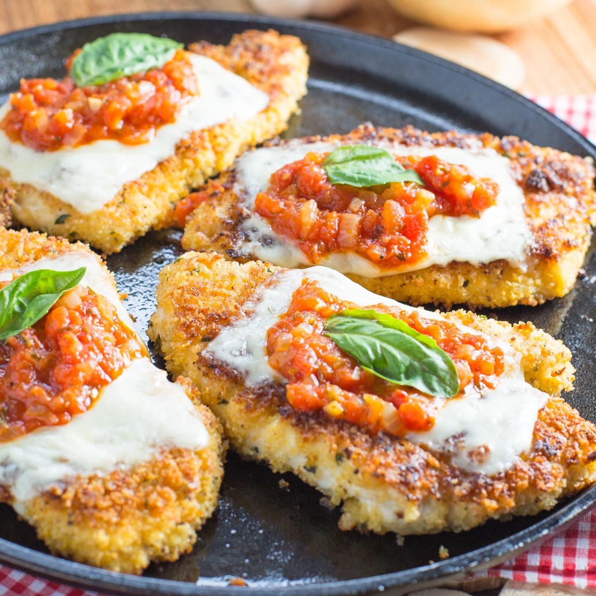 Cast iron skillet with chicken cutlets topped with marinara sauce melted cheese and fresh basil leaf.