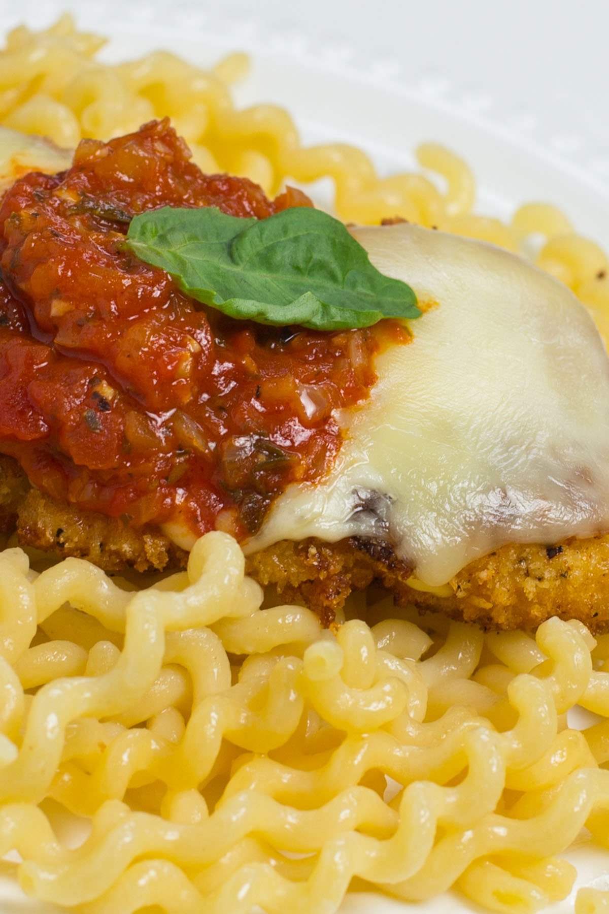 Chicken cutlet topped with melted cheese and marinara sauce on bed of pasta.