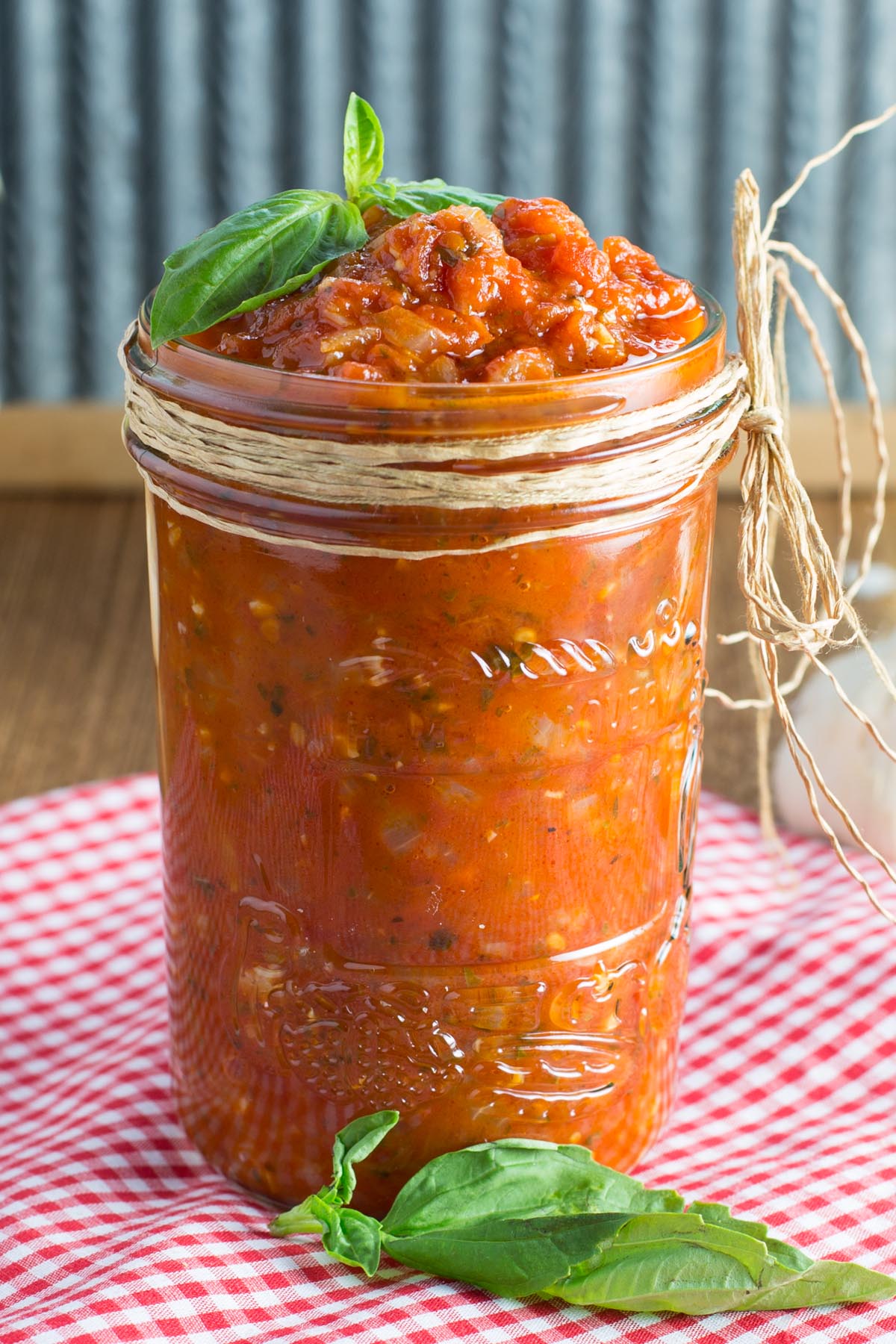 Homemade marinara sauce in glass jar decorated with basil leaves.