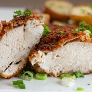 Roasted chicken breast cut in half on white plate garnished with green onion slices.