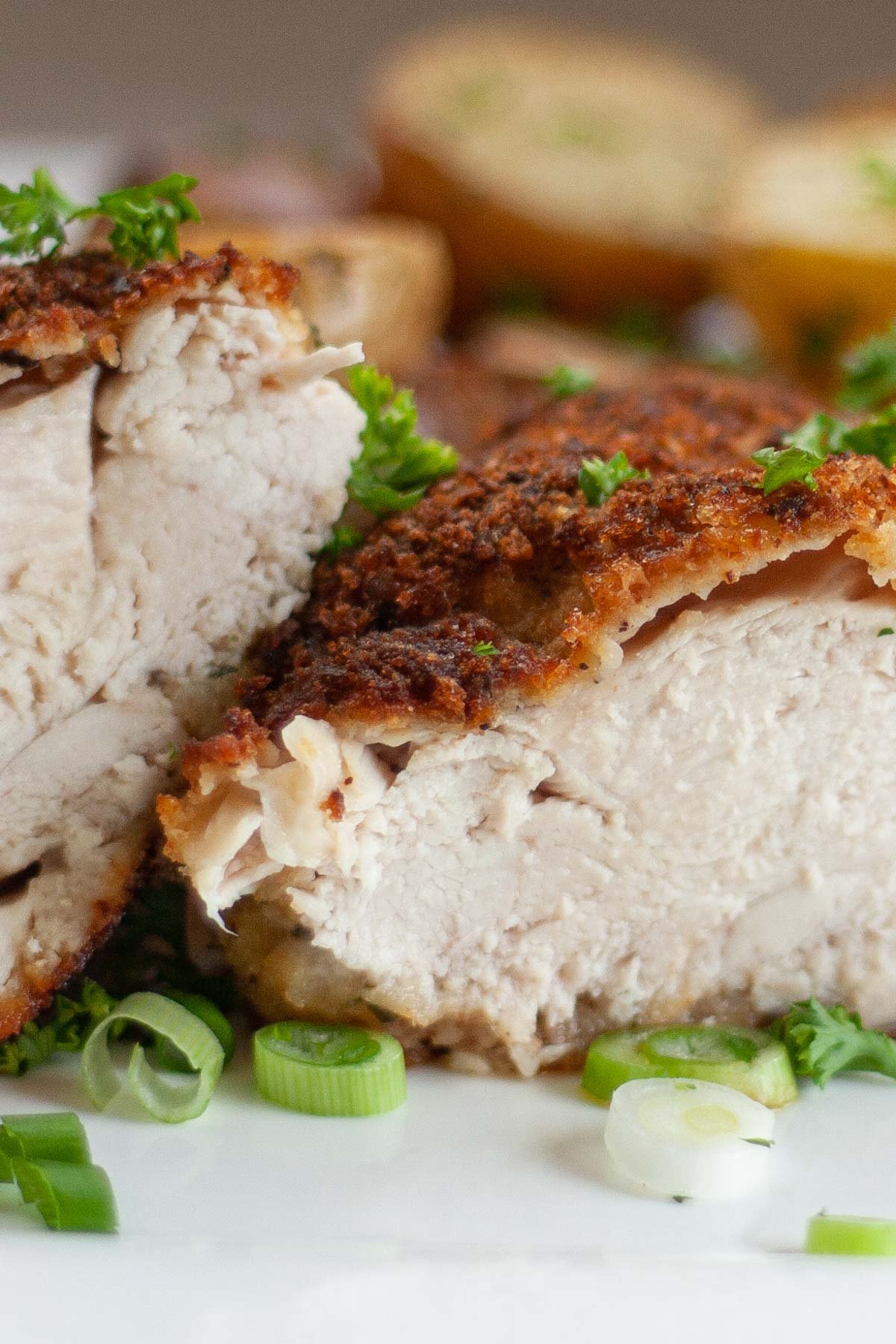 Roasted chicken breast cut in half on white plate garnished with green onion slices.