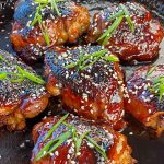 Baked chicken thighs glazed with teriyaki sauce, garnished with green onions and sesame seeds.