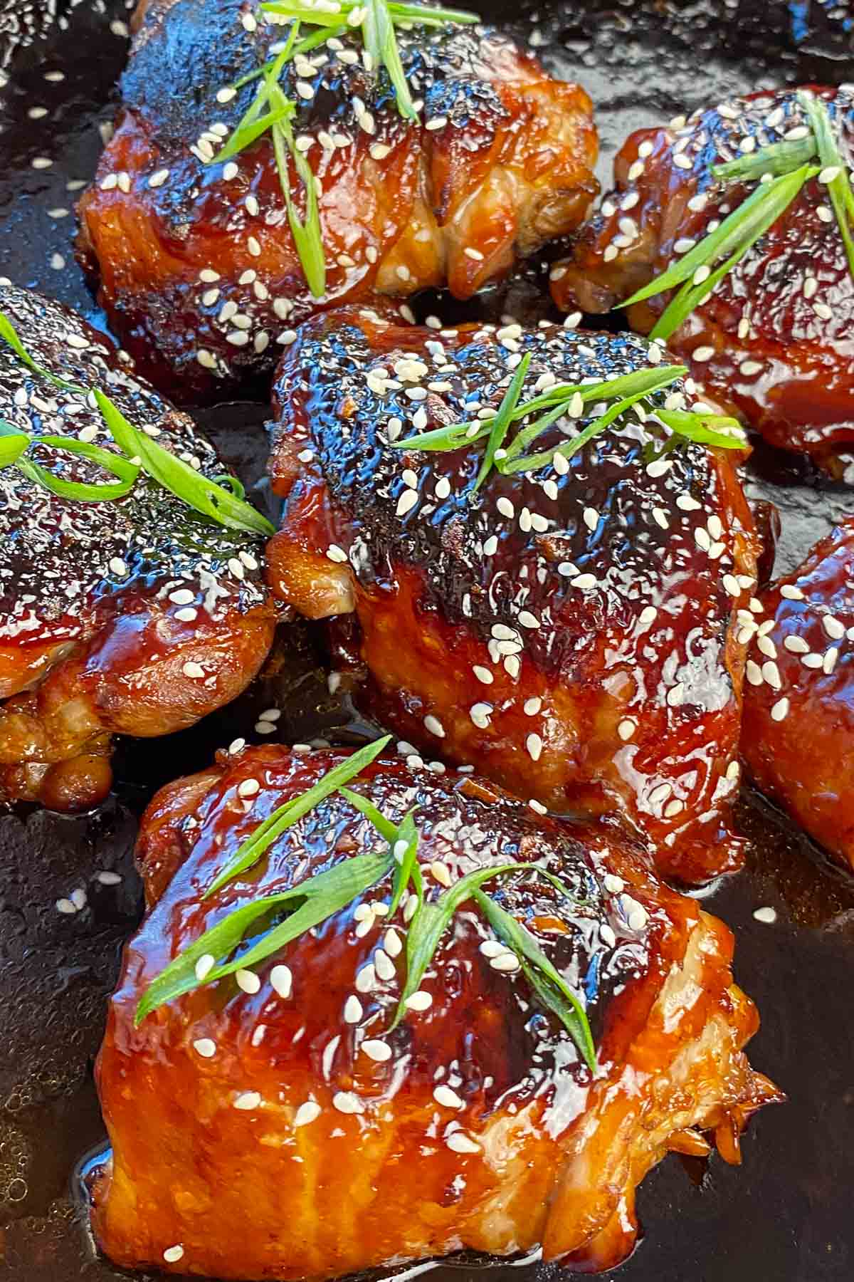 Baked chicken thighs glazed with teriyaki sauce, garnished with green onions and sesame seeds.