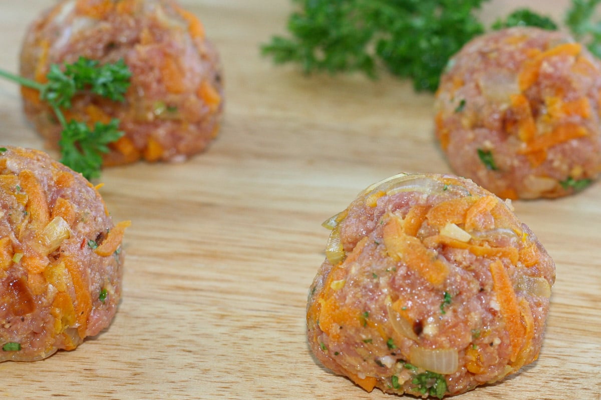 Uncooked meatballs made with on wood board.