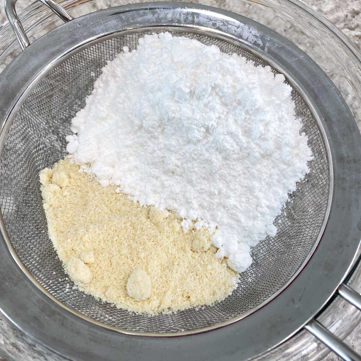 Confectioners' sugar and almond meal in a stainless steel sifter.