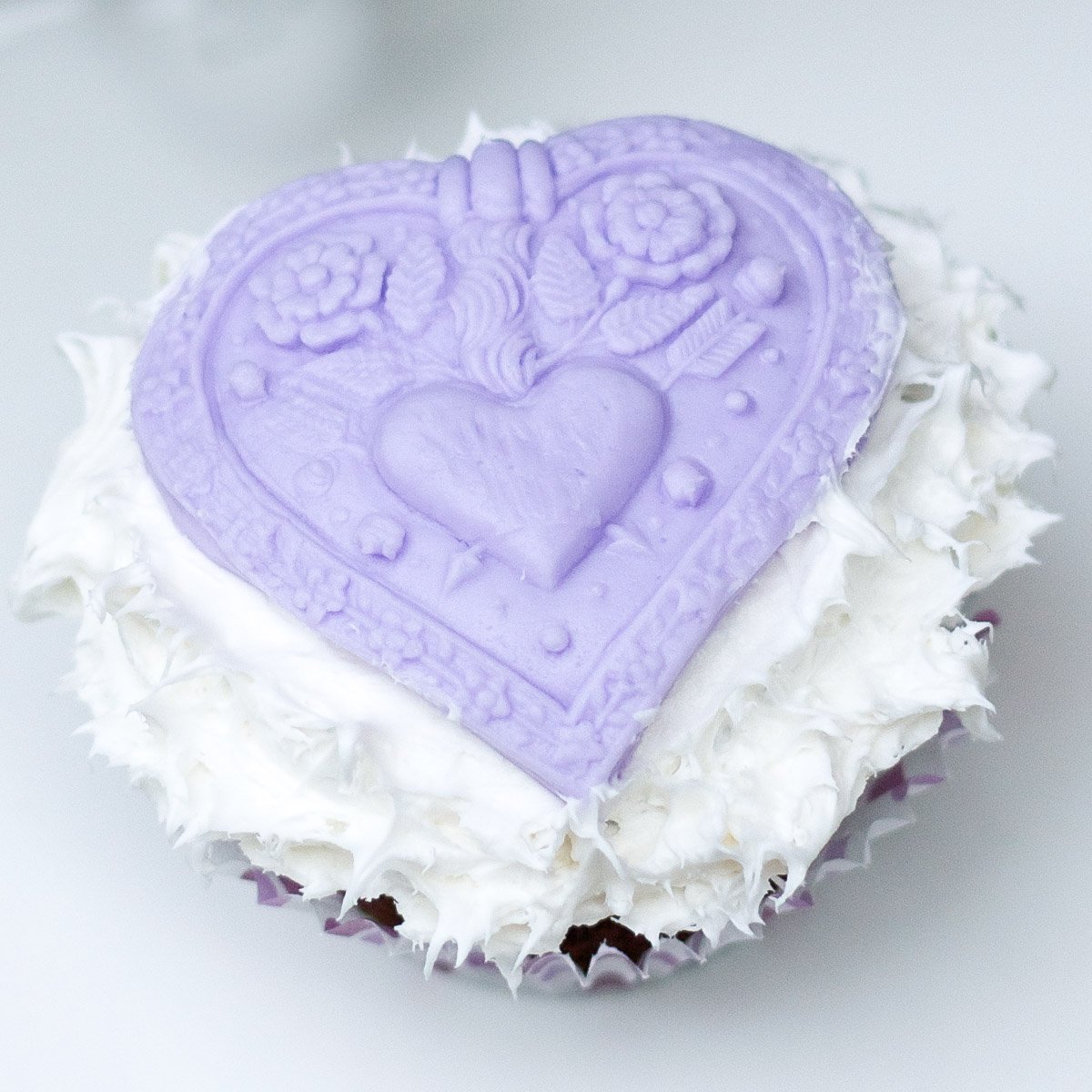 Chocolate cupcake with fluffy white icing top with purple fondant heart decoration.