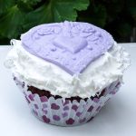 Chocolate cupcake with fluffy white icing top with purple fondant heart decoration.