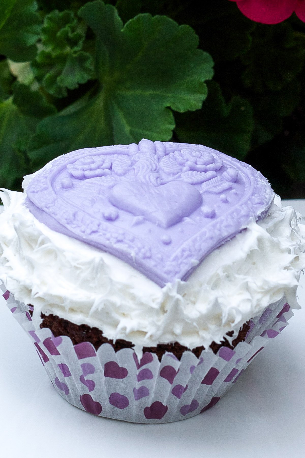 Chocolate cupcake with fluffy white icing top with purple fondant heart decoration.