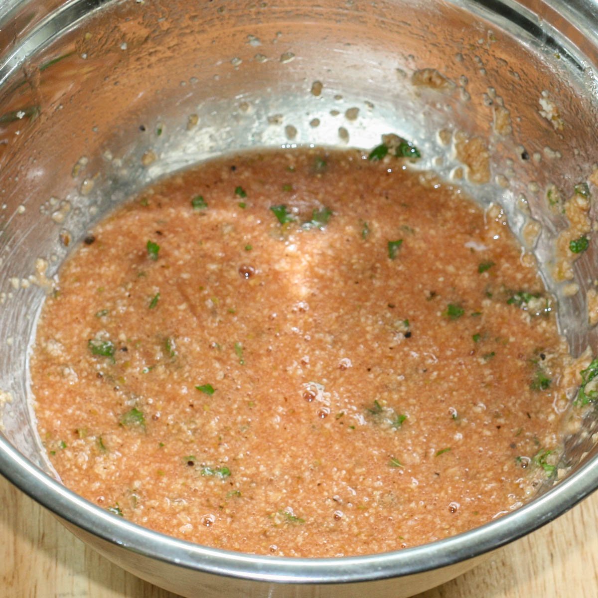 Stainless steel bowl filled with mixture of eggs, tomato juice, breadcrumbs and herbs.