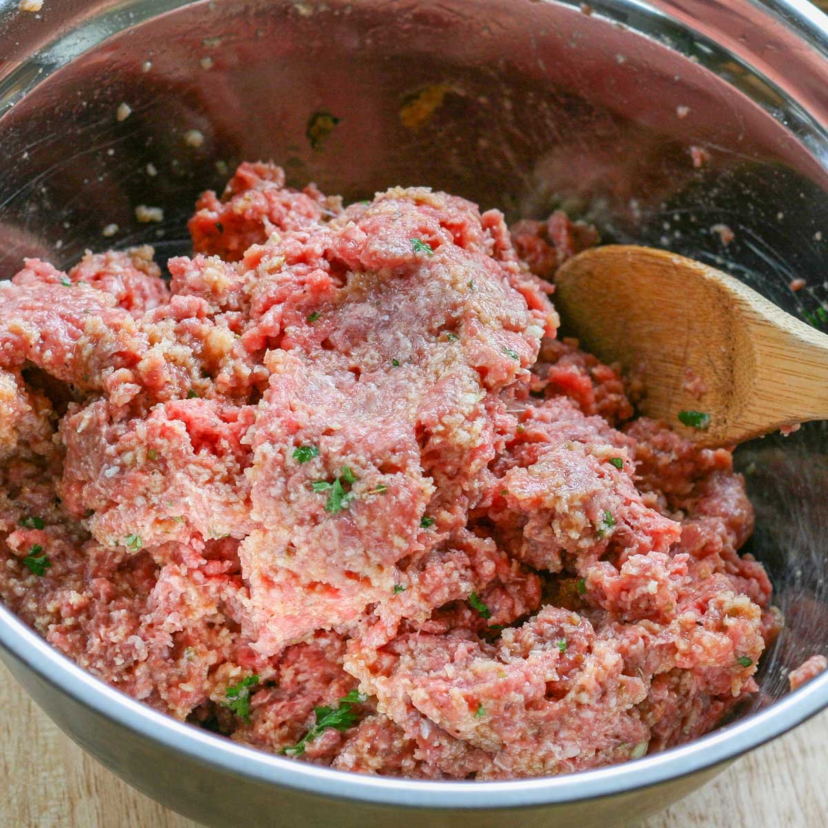 Mixture of ground beef and spices in a stainless steel bowl.