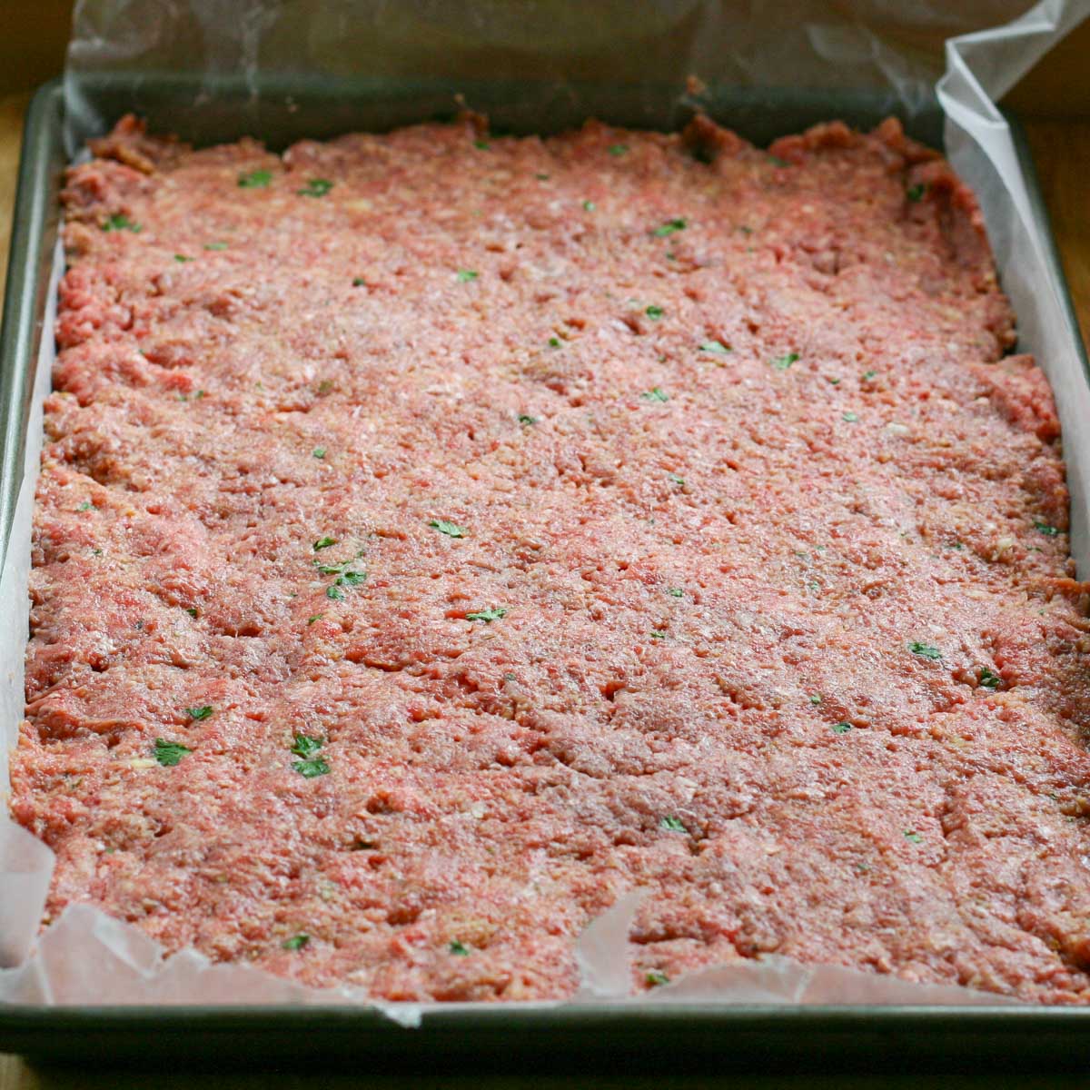 Meatloaf mixture pressed into a waxed paper lined baking sheet.