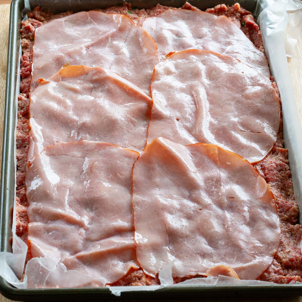 Ground beef mixture in baking sheet topped with ham slices.