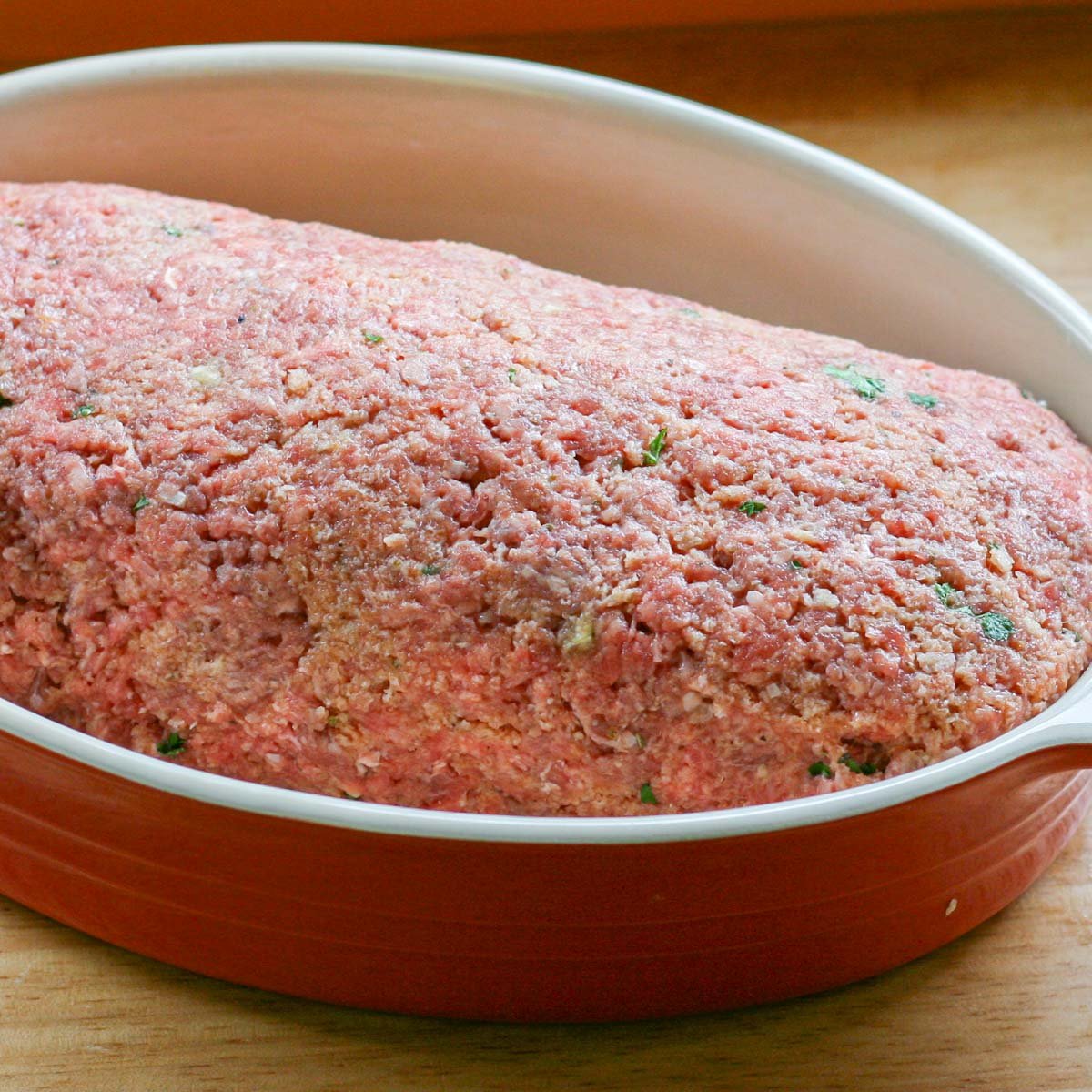 Uncooked meatloaf in red oval baking dish.