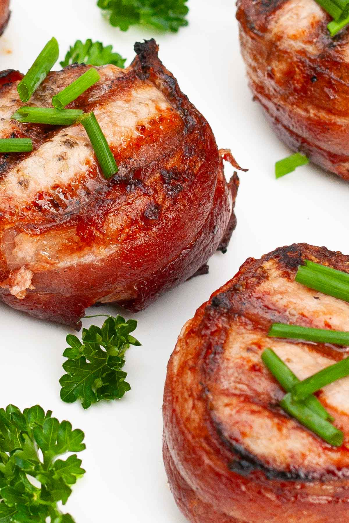 Pork medallions with bacon garnished with green onions on a white plate.