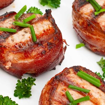 Pork medallions with bacon garnished with green onions on a white plate.