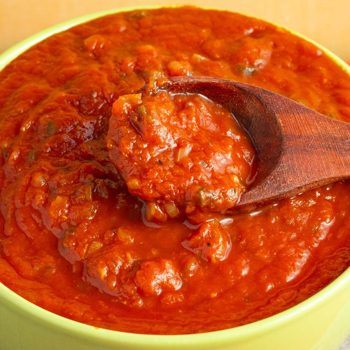 Yellow bowl of enchilada sauce with wood spoon in it.