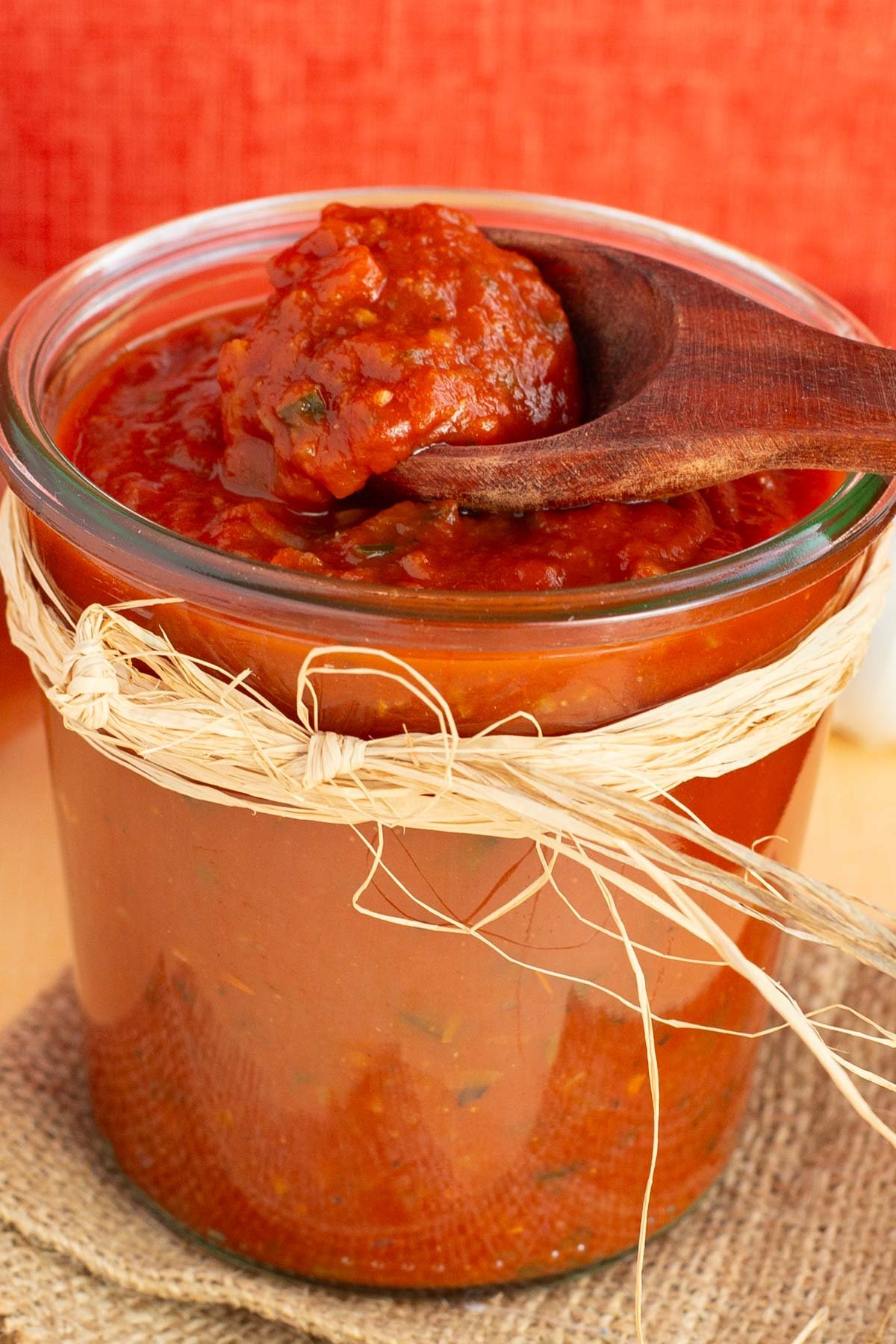 Wooden spoon scooping sauce from glass jar filled with enchilada sauce.