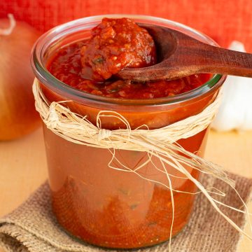 Wooden spoon scooping sauce from glass jar filled with enchilada sauce.