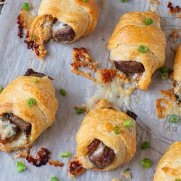 Appetizers of steak and bluecheese wrapped in crescent rolls on parchment paper.