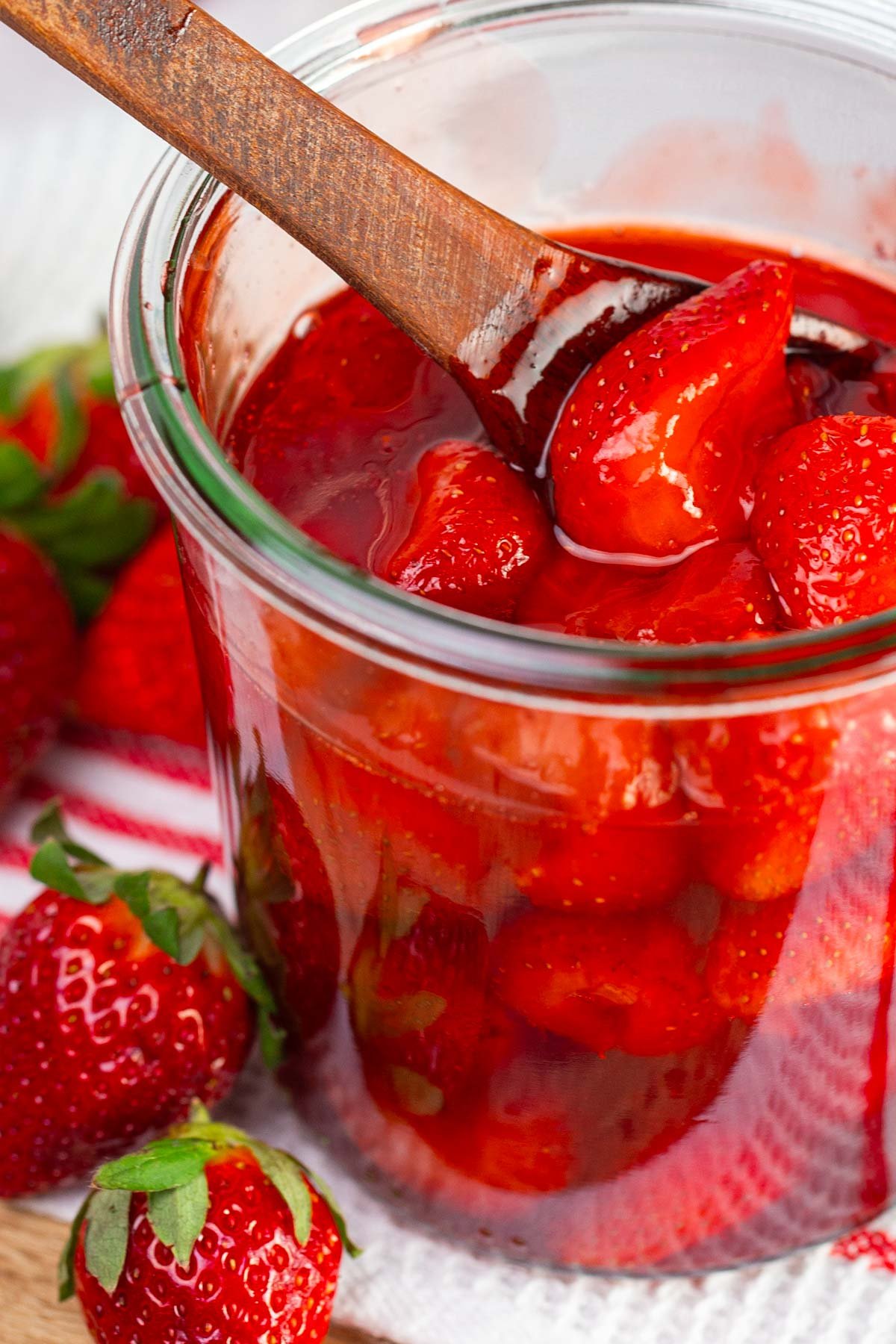 Chunky strawberry sauce in glass jar with wooden spoon.