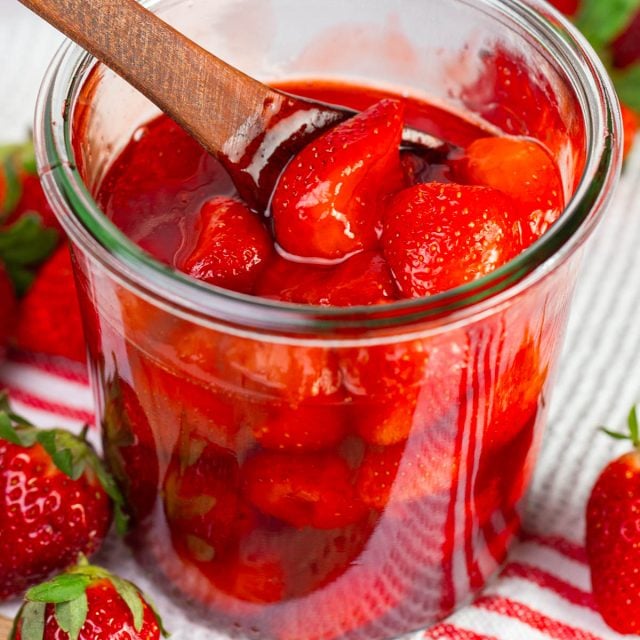 Chunky strawberry sauce in glass jar with wooden spoon.