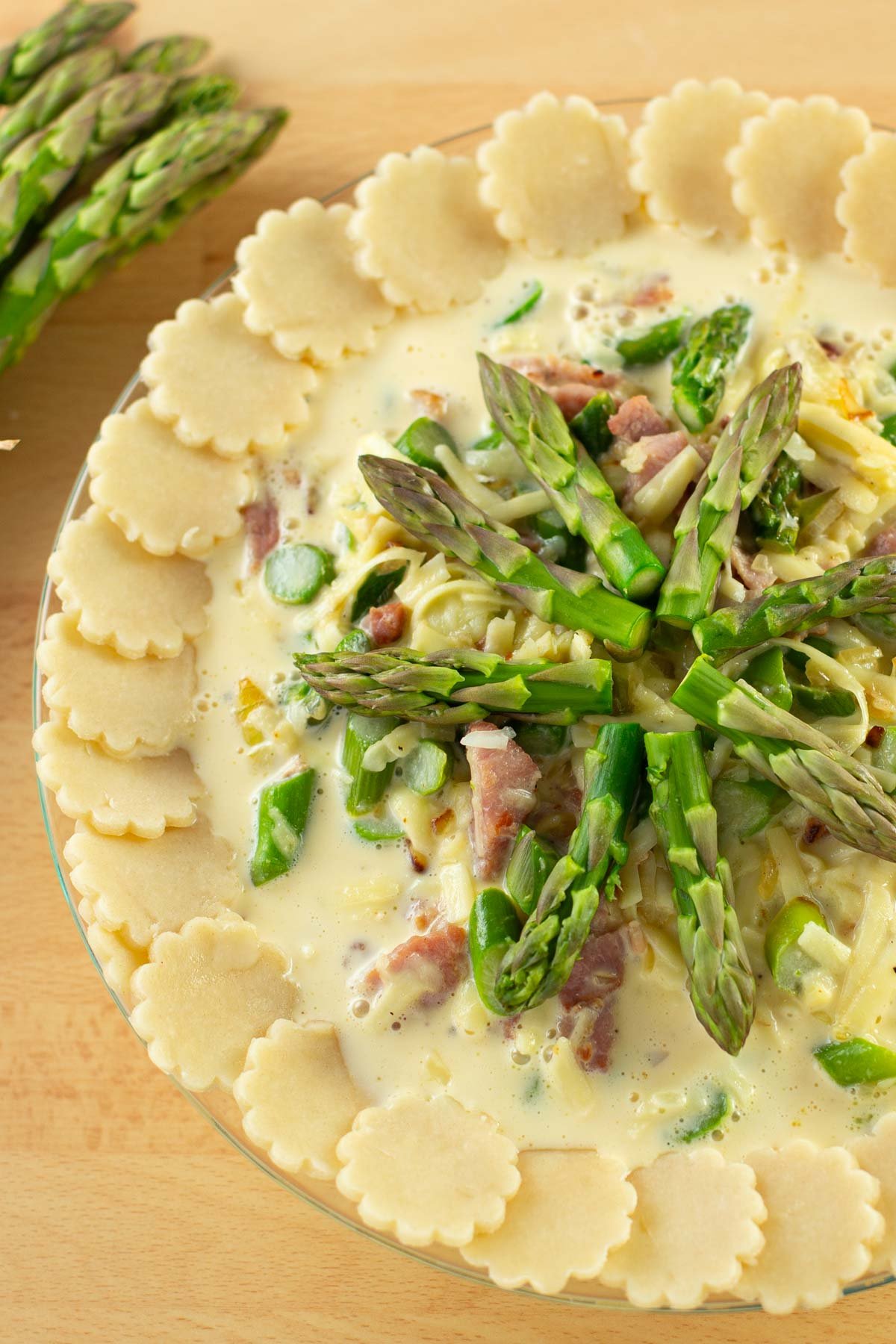 Unbaked asparagus quiche in glass pie plate.