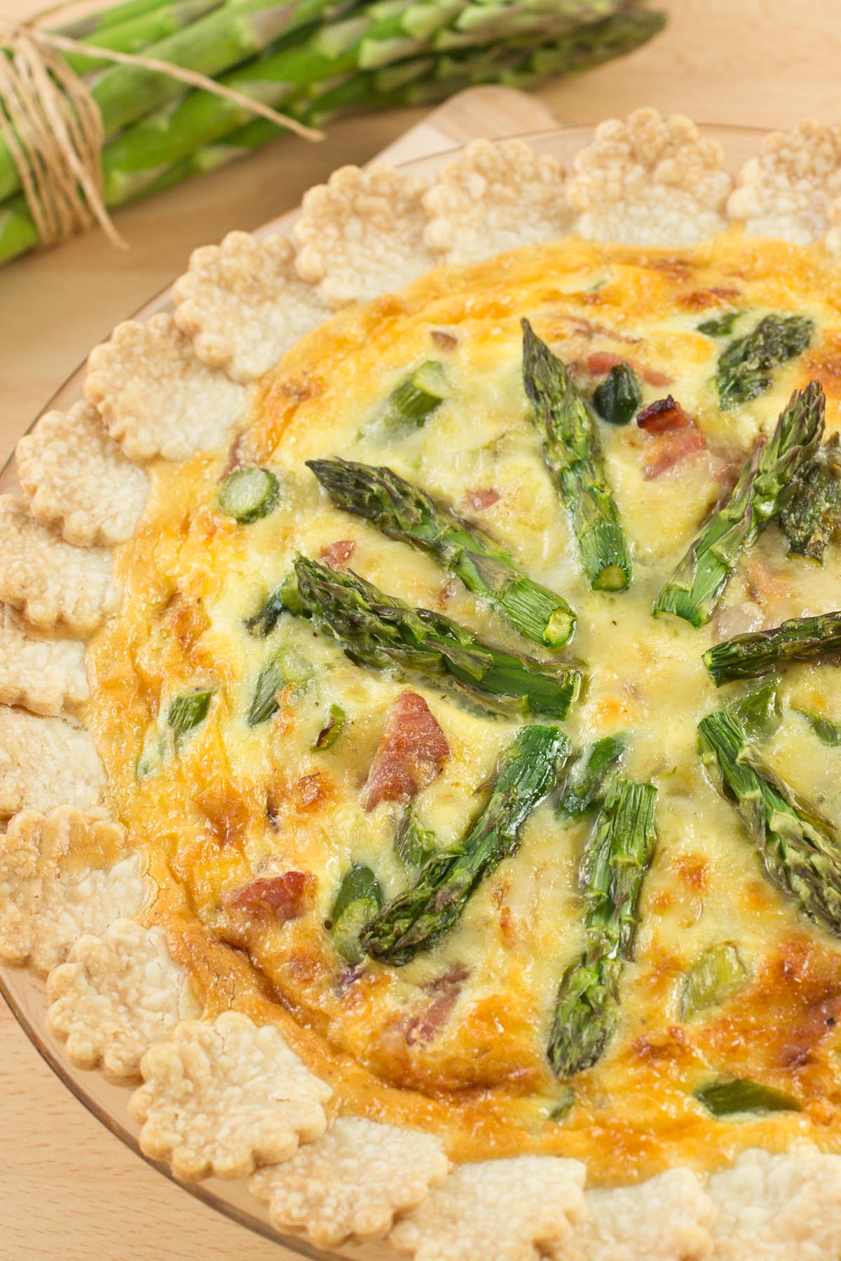 Slice of fresh Asparagus and Gruyere Cheese Quiche on a white plate.