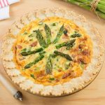 Quiche topped with asparagus spears in glass pie plate.