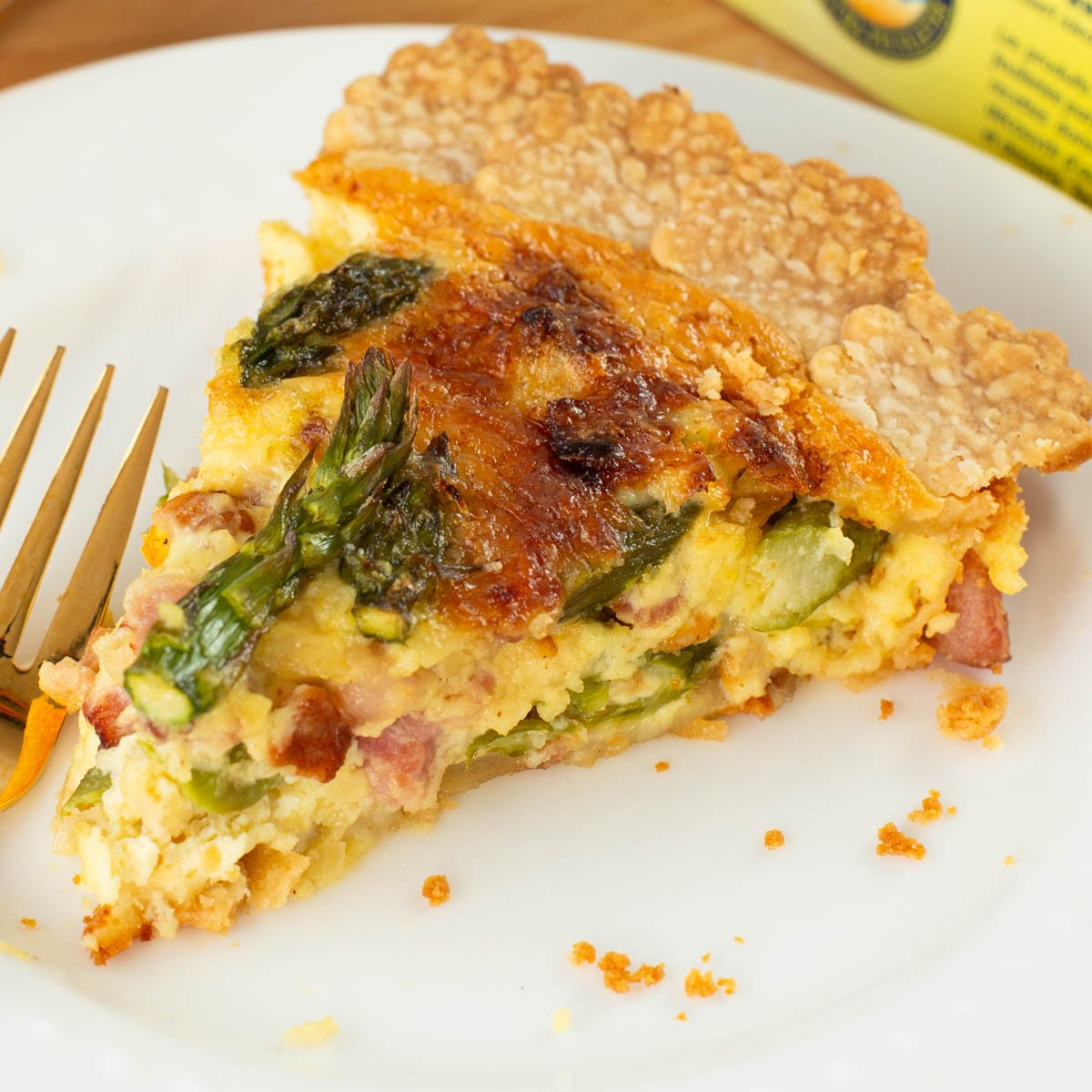 Slice of fresh asparagus and gruyere cheese quiche on white plate.