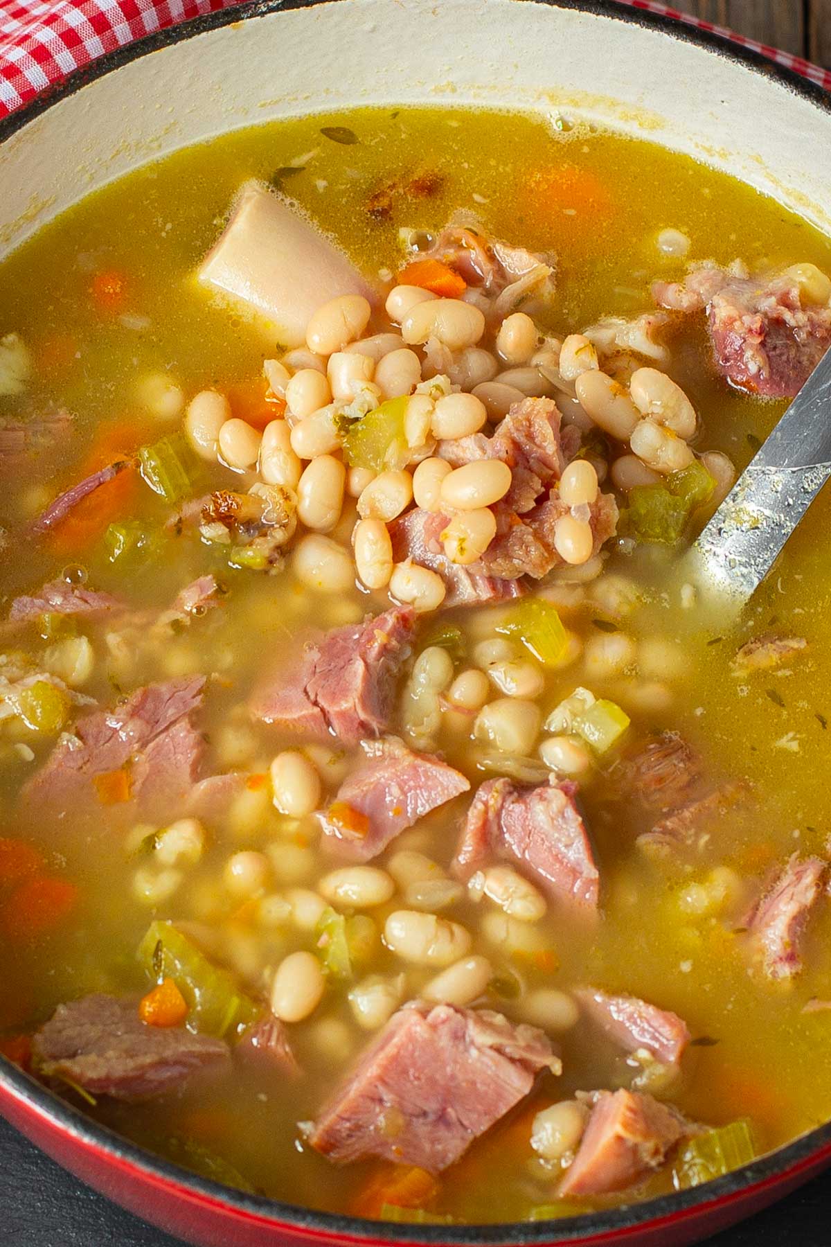 Cooking pot of soup with chunks of ham, a ham hock, beans and vegetables.