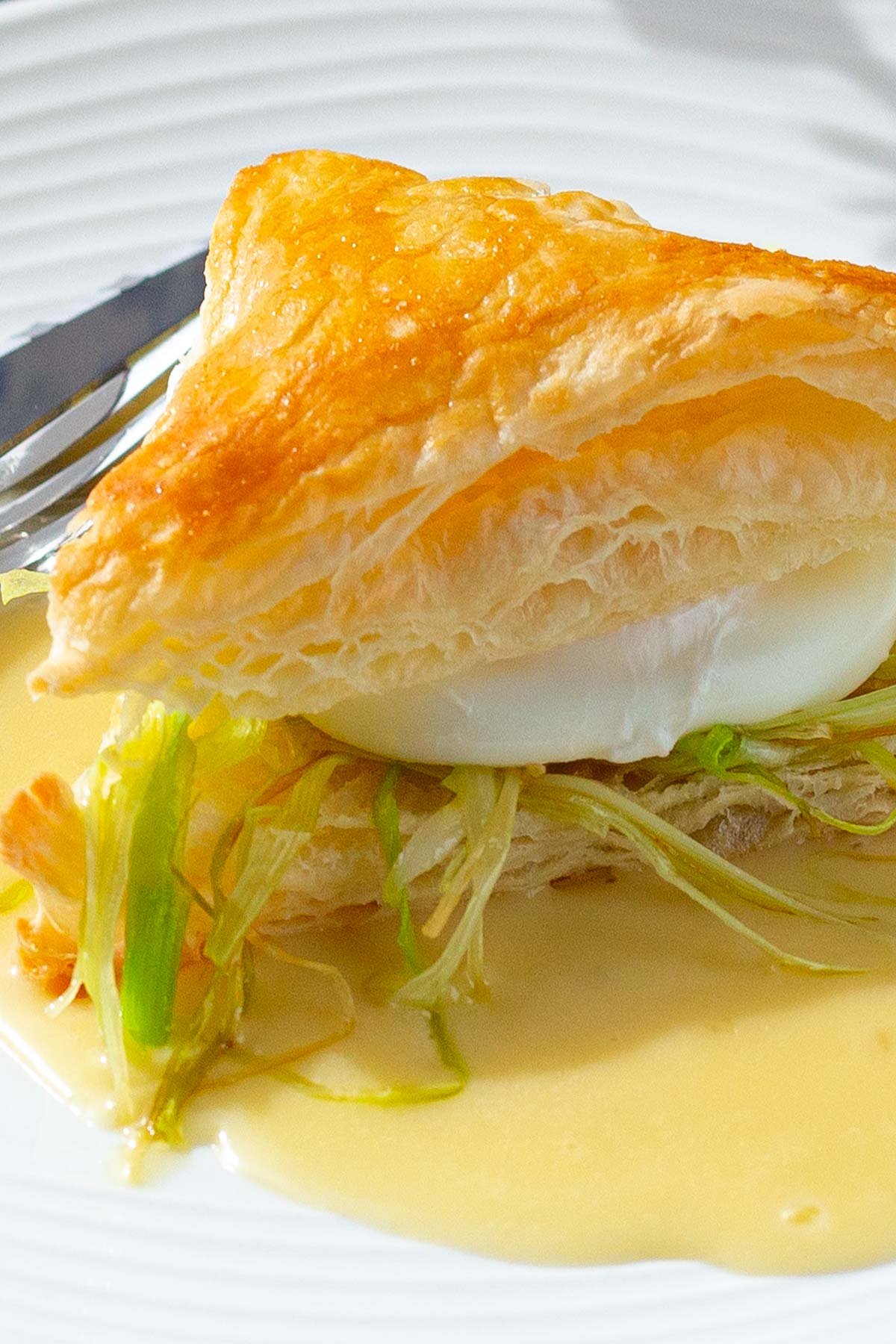 Puffed pastry sandwich with cooked julienned leeks and a poached egg on bed of butter sauce.