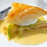 Puffed pastry sandwich with cooked julienned leeks and a poached egg on bed of butter sauce.