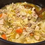 A hearty turkey noodle soup with chunks of turkey, carrots, celery and egg noodles served with copper ladle.