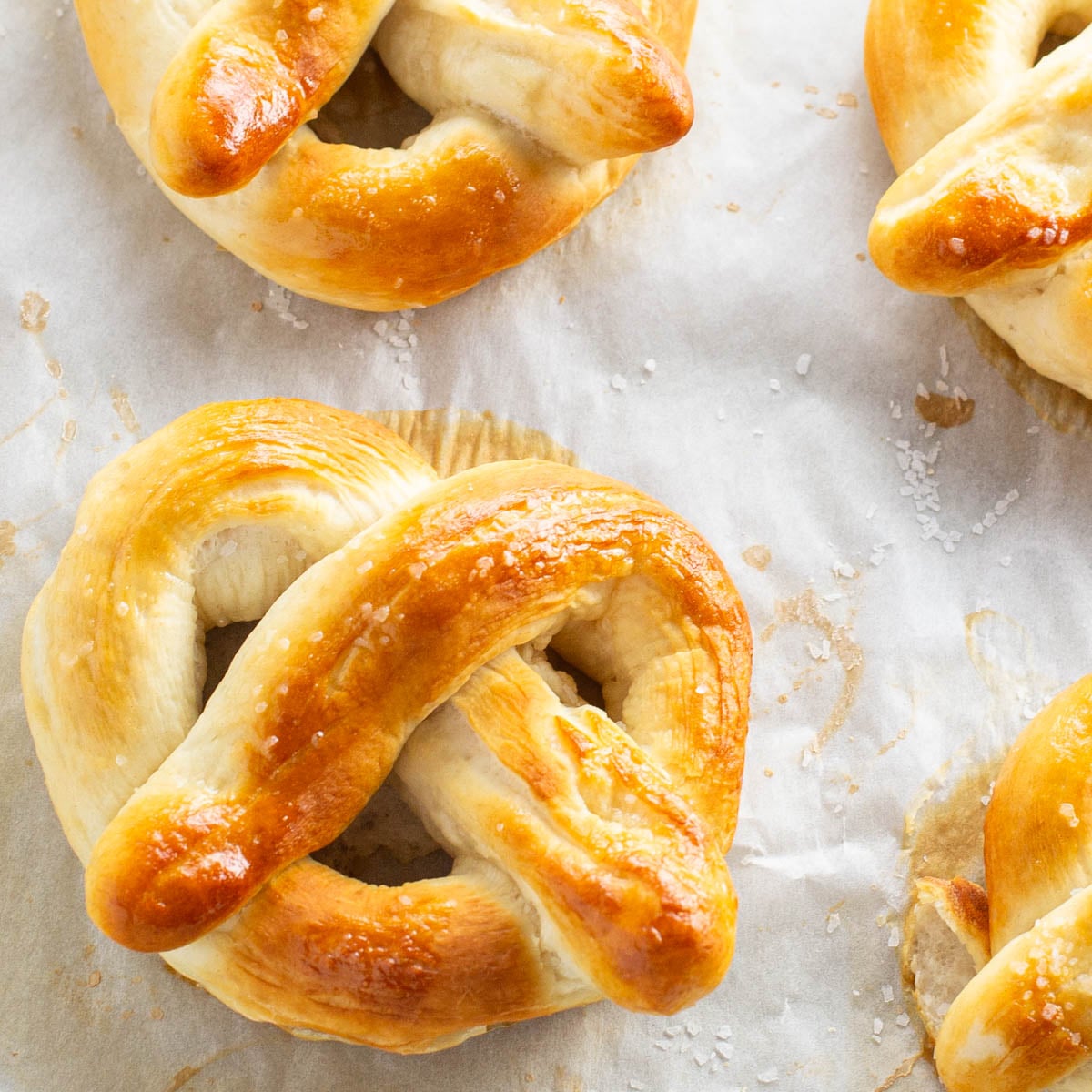 Golden-brown pretzels sprinkled with coarse salt, resting on parchment paper.