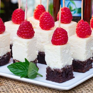 Squares of cheesecake with brownie crust, topped with a fresh raspberry.
