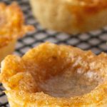 Golden brown butter tarts with flaky crusts sit on a black cooling rack.