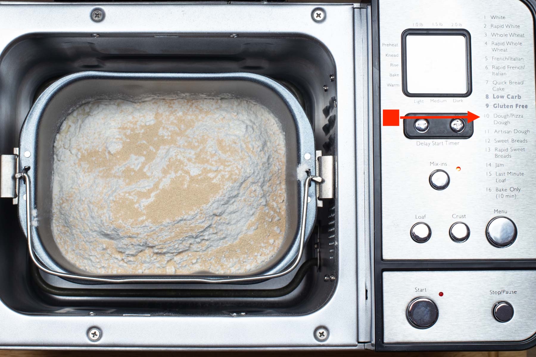 Bread machine with lid open, showing the ingredients inside the pan. Control panel on the right side displays "Dough" setting.
