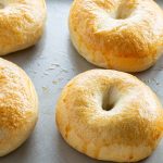 Freshly baked bagels with a golden, glossy crust on a baking tray.
