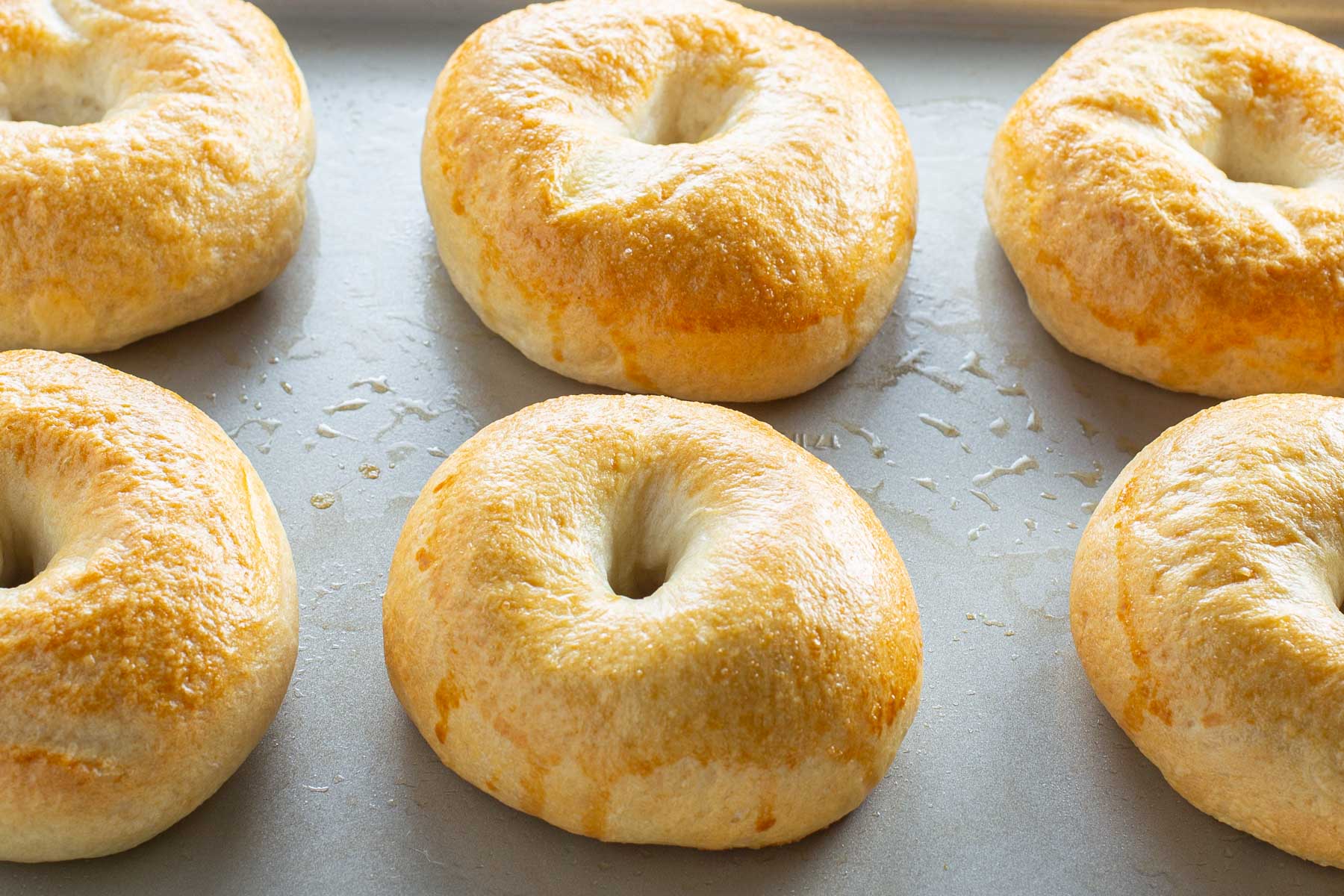 Freshly baked bagels with a golden, glossy crust on a baking tray.