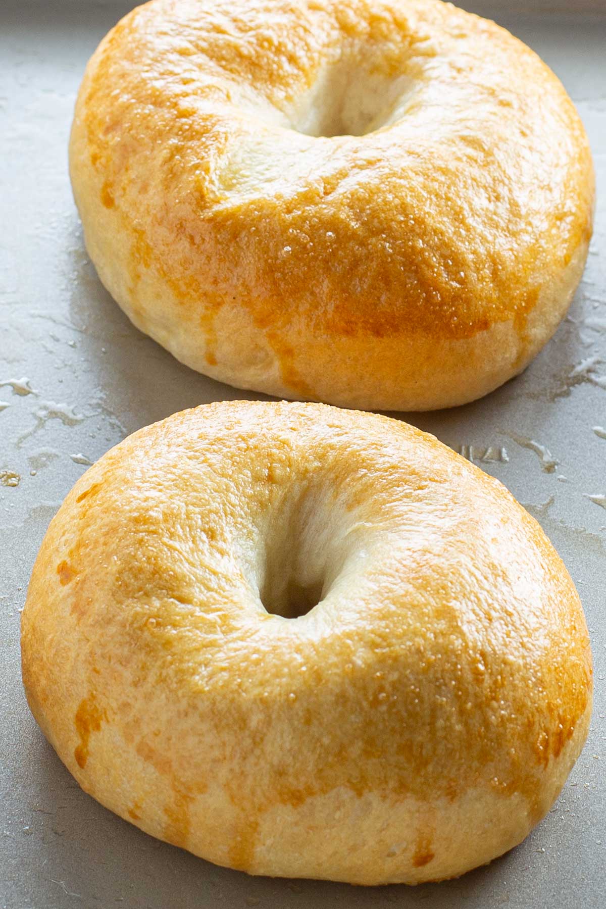 Freshly baked bagels with a golden, glossy crust on a baking tray.