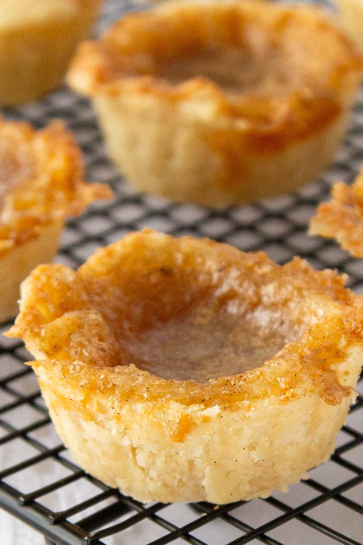 Golden brown butter tarts with flaky crusts sit on a black cooling rack.