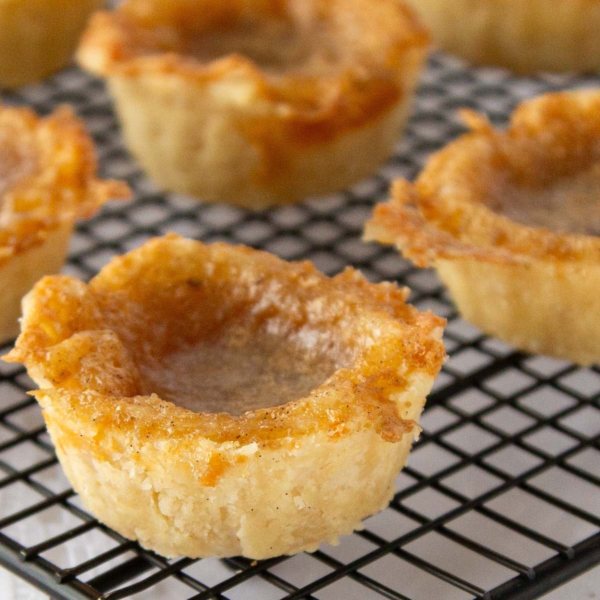 Golden brown butter tarts with flaky crusts sit on a black cooling rack.