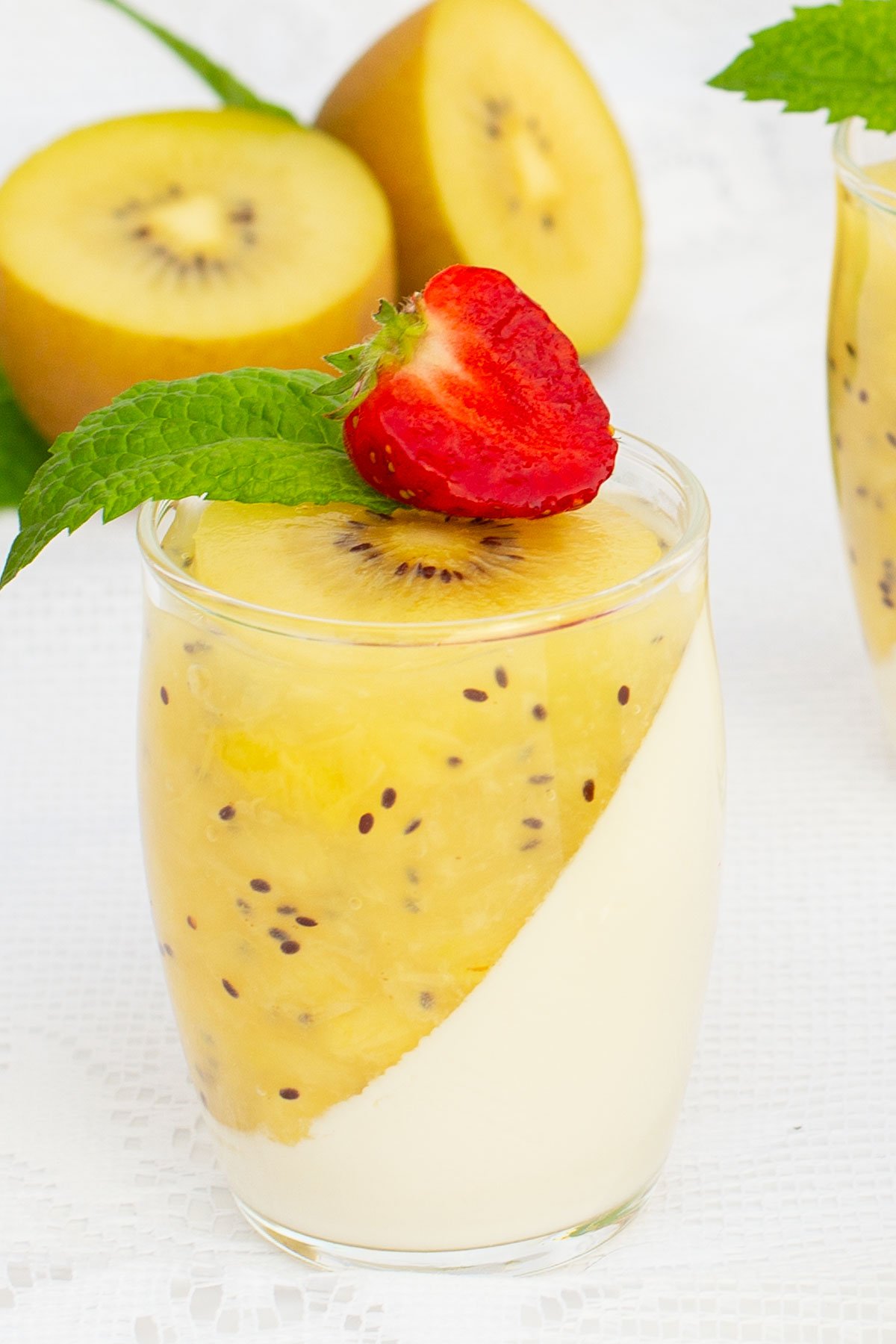 Elegant dessert glasses filled with creamy panna cotta, topped with a diagonal layer of kiwi puree. Garnished with fresh strawberries and mint leaves