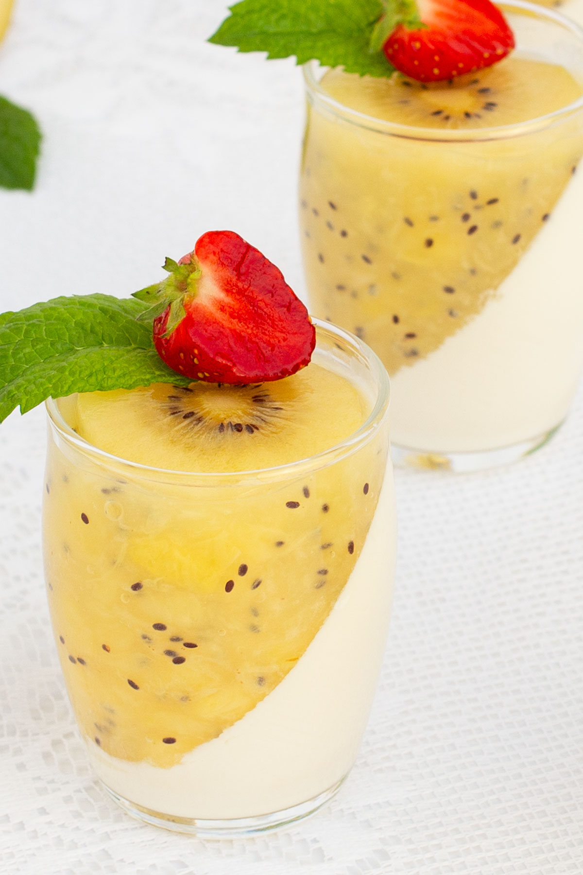 Elegant dessert glasses filled with creamy panna cotta, topped with a diagonal layer of kiwi puree. Garnished with fresh strawberries and mint leaves
